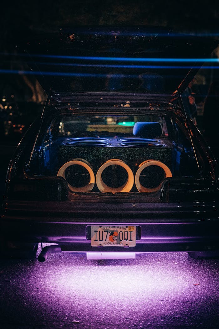 A modified car trunk featuring a powerful sound system with neon underglow lighting at night.